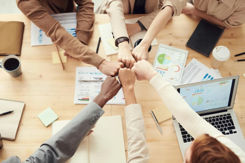 Personas uniendo los puños sobre una mesa de trabajo con gráficos, representando alianzas estratégicas y colaboración en proyectos digitales.
