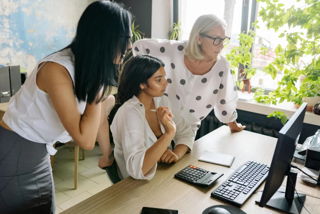 Tres mujeres latinas colaborando frente a una computadora, representando capacitación, inclusión y inteligencia artificial, comunidad latina.